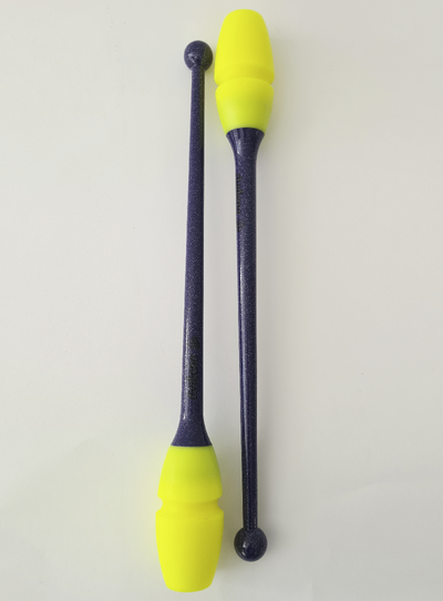 Para maczug do gimnastyki artystycznej w kolorach: fioletowym, żółtym z brokatem; ułożone równolegle i skierowane w przeciwne strony.